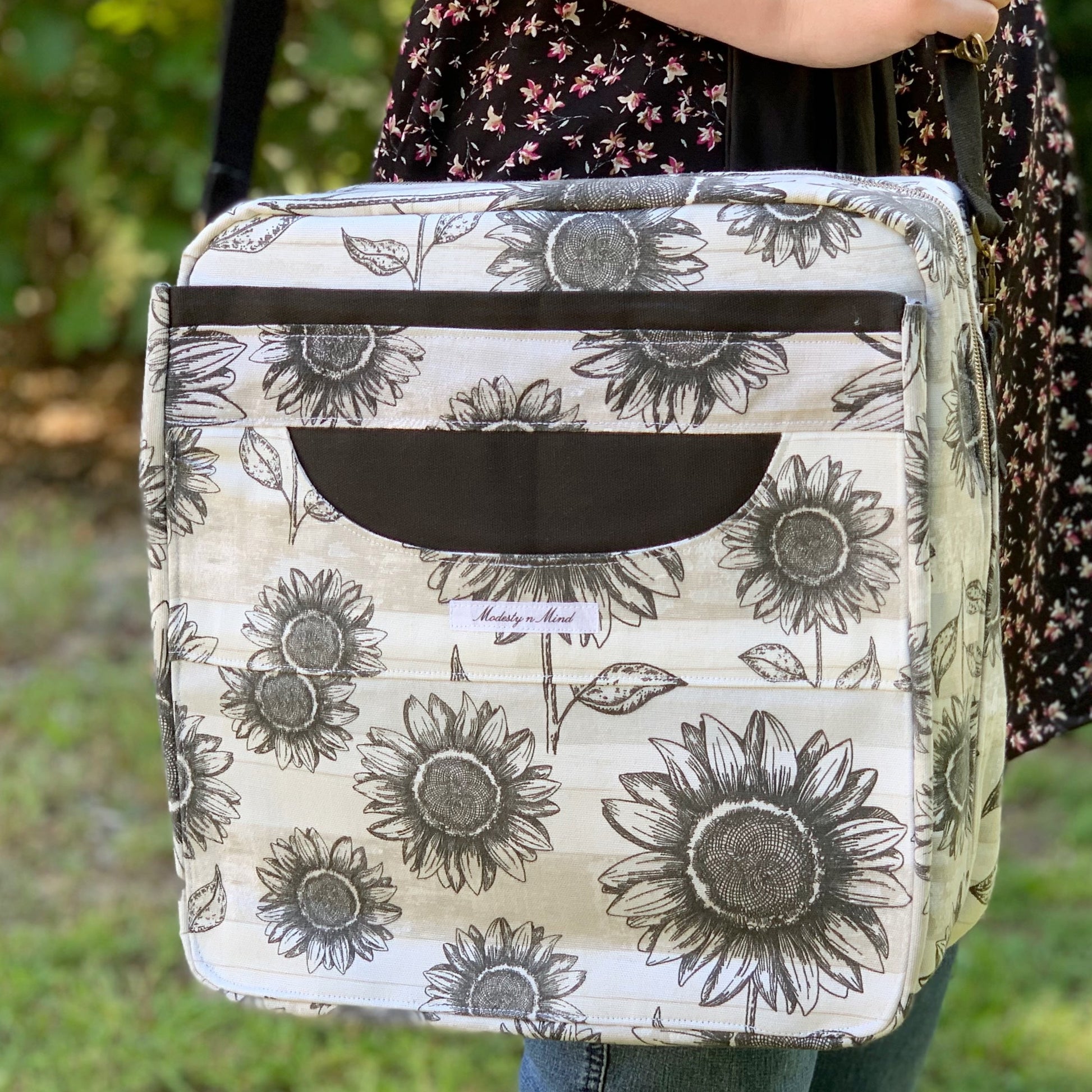 A tote bag with a floral pattern, featuring a front zippered compartment and a strap.