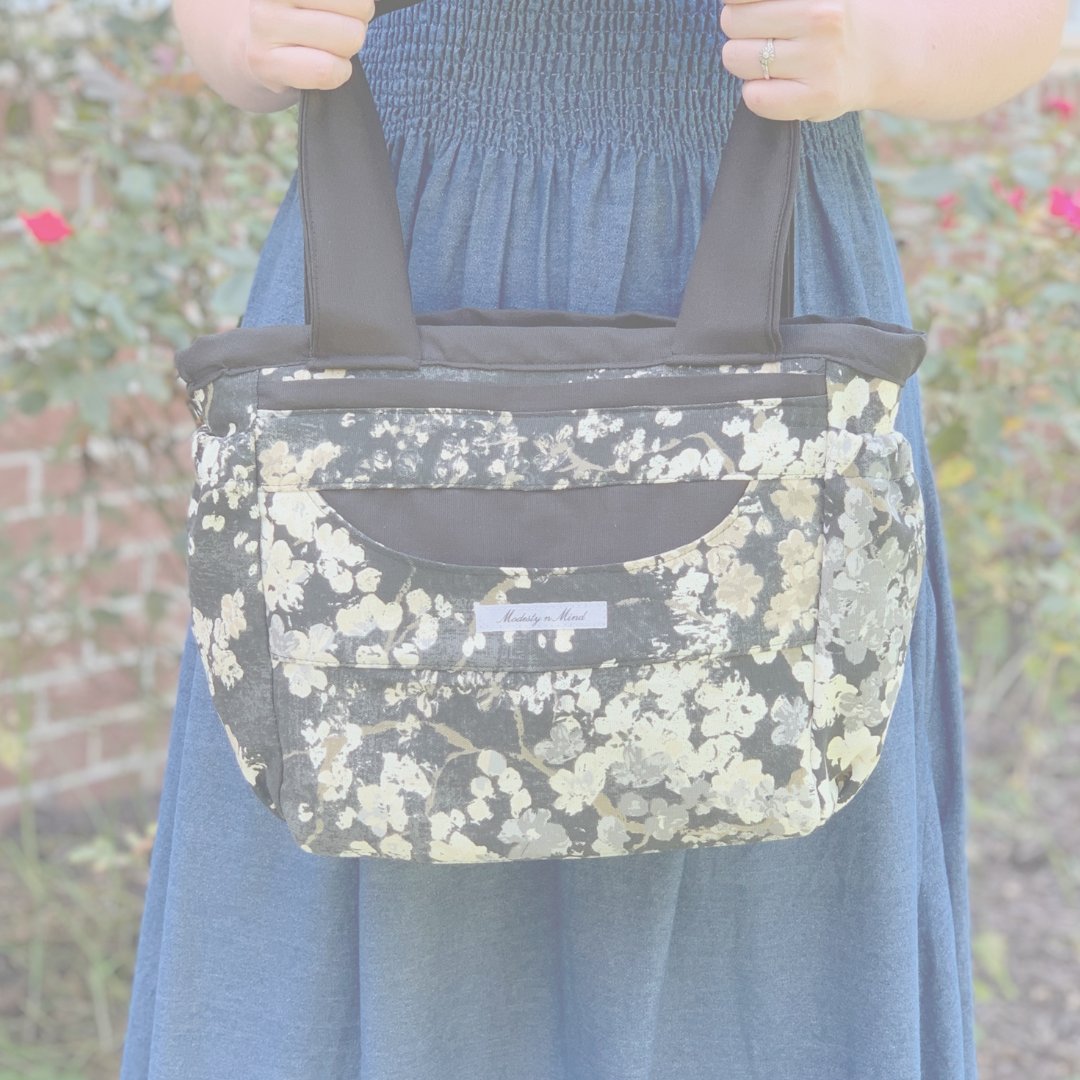 Gray Beige Floral tote bag held in front of a rose bush