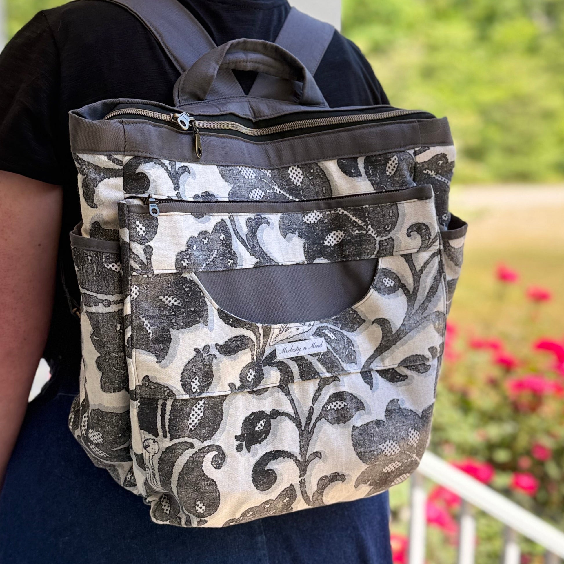 Person wearing a floral-patterned backpack on a porch with flowers in the background