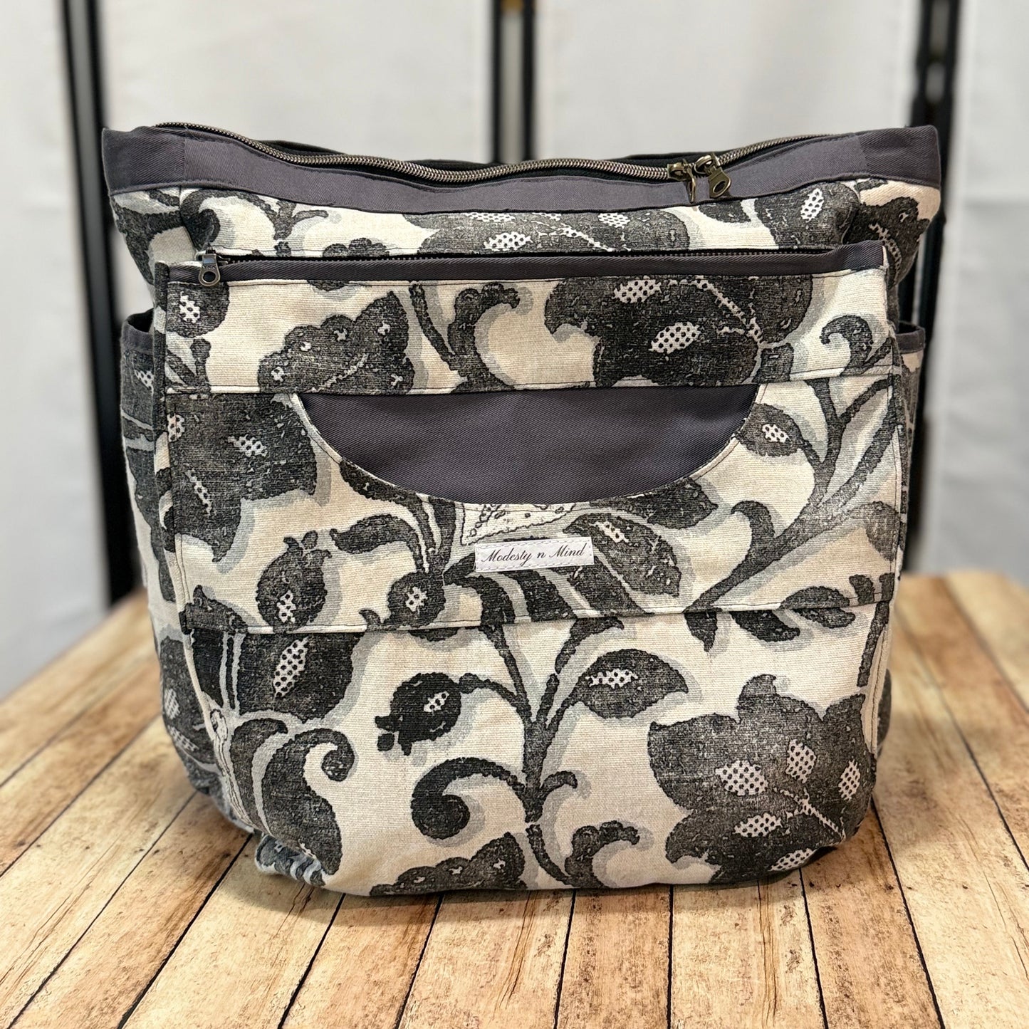 Floral patterned back pack  with gray flowers on a white background, placed on a wooden surface.