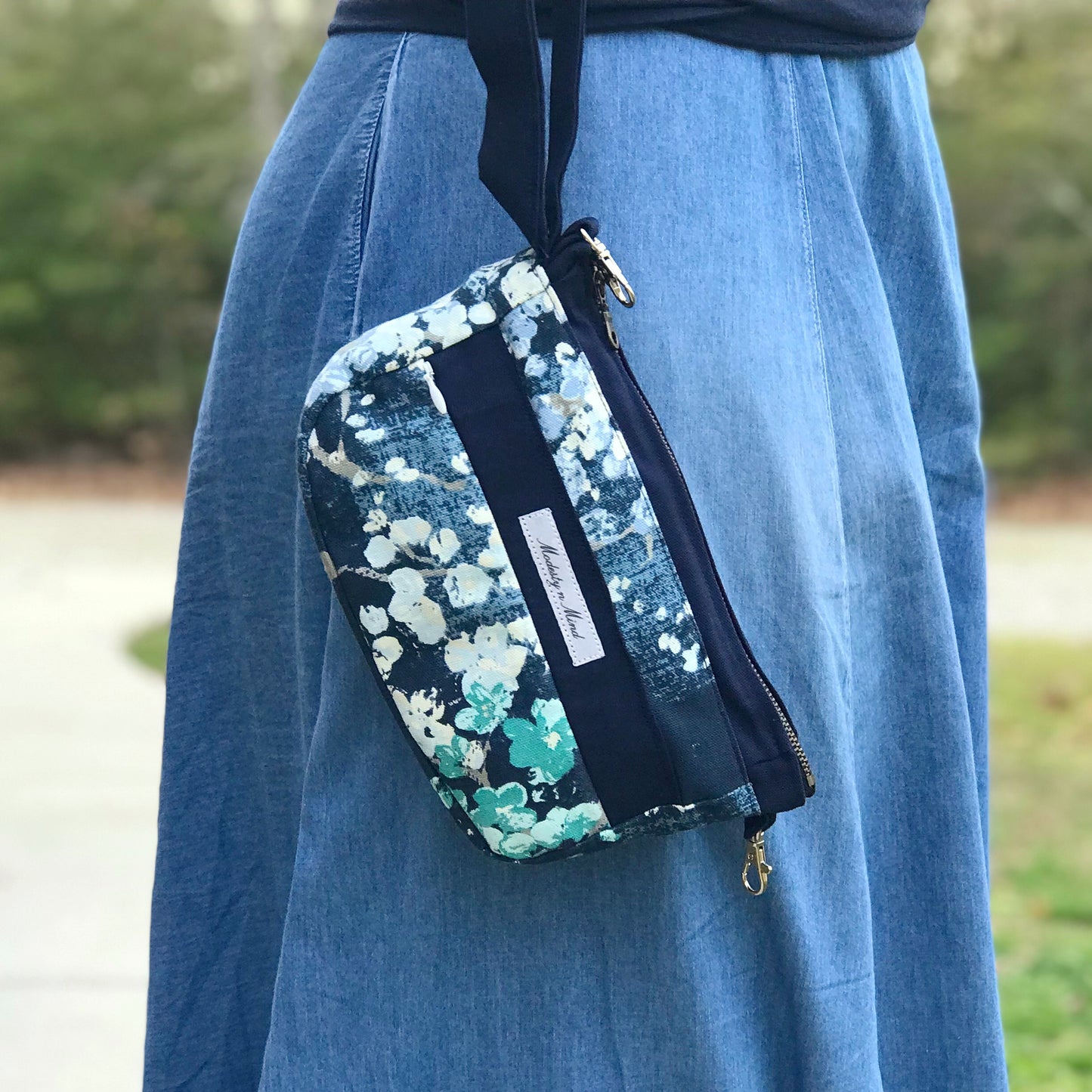 Image of blue floral wristlet being held outside with trees in the background
