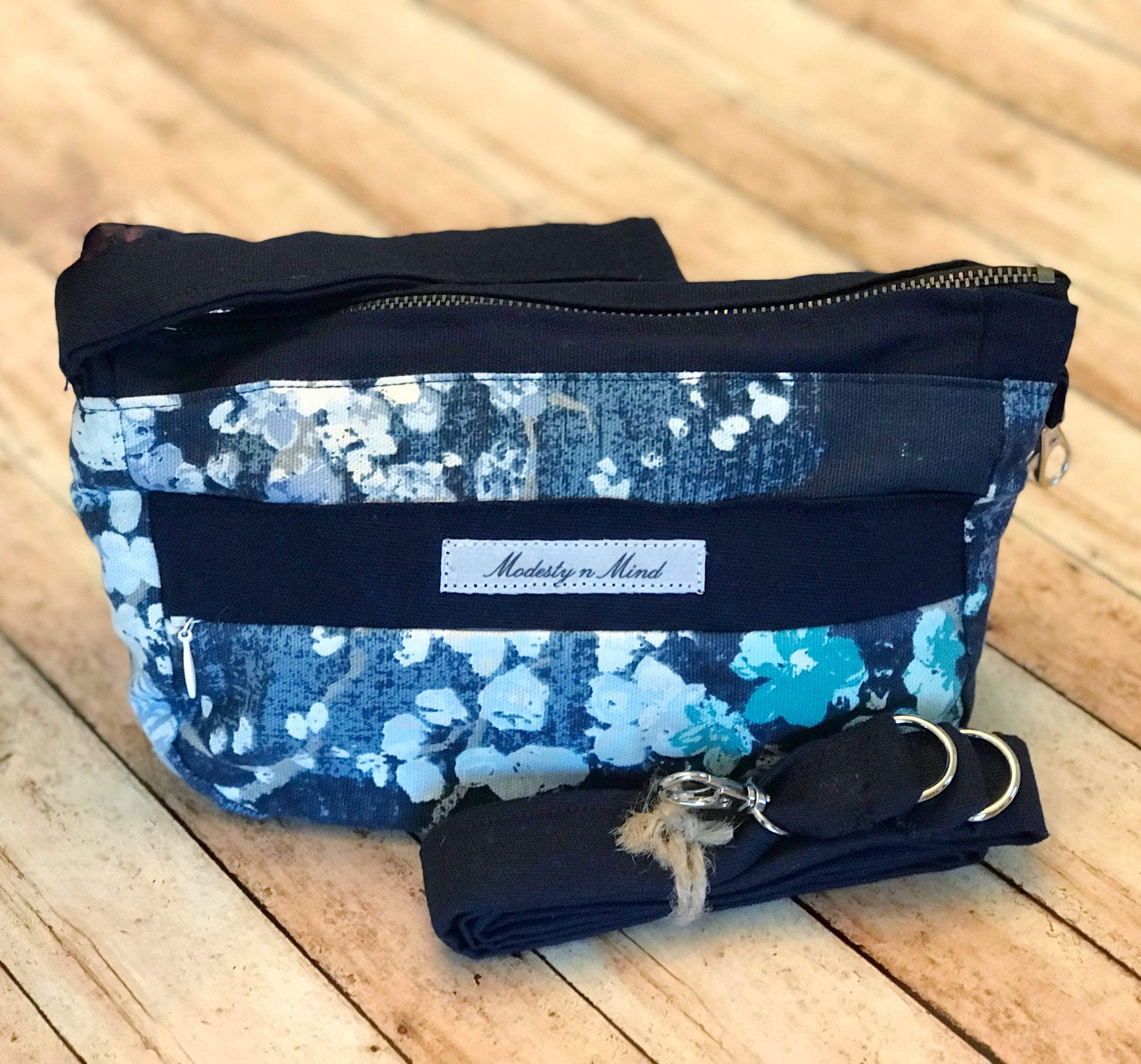 Blue teal floral wristlet sitting on backdrop with a navy blue strap leaning against it.